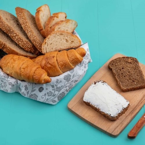 side-view-breads-as-sliced-seeded-cob-baguette-croissant-bowl-rye-bread-smeared-with-cheese-cutting-board-with-knife-blue-background_11zon.jpg